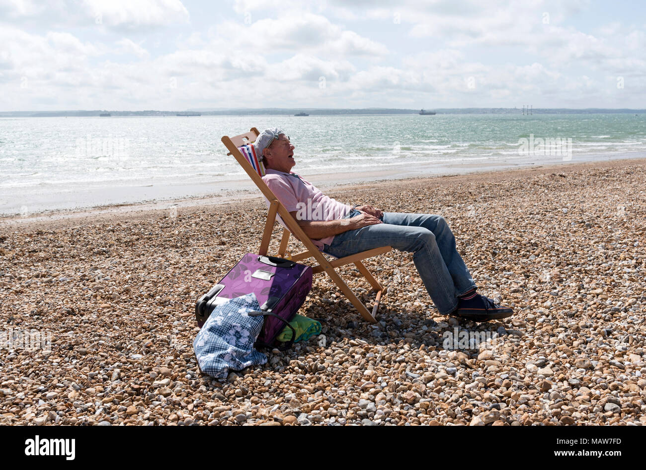 Uomo anziano che indossa un fazzoletto annodato sulla sua testa rilassante sulla spiaggia. Southsea, England Regno Unito Foto Stock