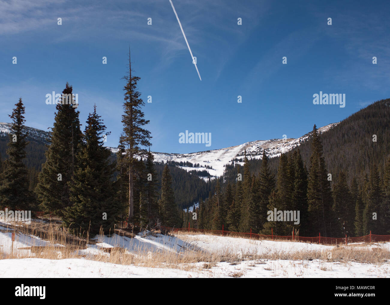 Prato Nevoso paesaggio con Snow-Capped montagne sullo sfondo, Contrail nel luminoso cielo blu, al Parco Nazionale delle Montagne Rocciose in Colorado Foto Stock