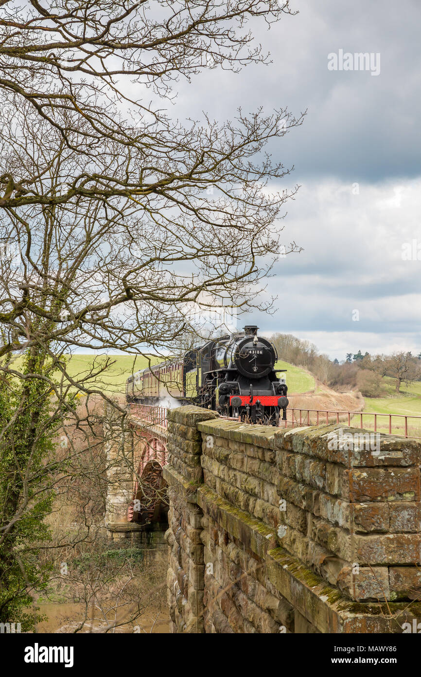 Vista frontale della vecchia, vintage UK locomotiva a vapore 43106 (LMS Ivatt Classe 4) avvicinando, sbuffando fumo, viaggiando attraverso la paesaggistica campagna in primavera. Foto Stock