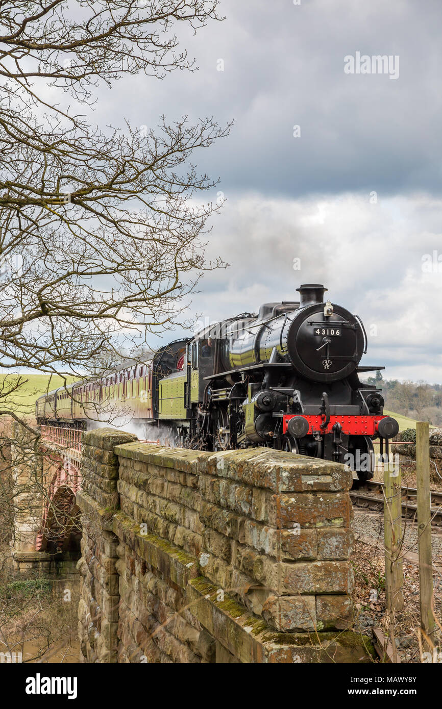 Vista frontale della vecchia, vintage SVR locomotiva a vapore 43106 (LMS Ivatt Classe 4) avvicinando, sbuffando fumo, viaggiando attraverso la paesaggistica campagna in primavera. Foto Stock