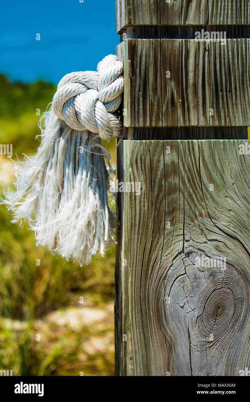 Pulire annodato Corda bianca con una estremità sfilacciata sporgente attraverso un palo di legno all'aperto presso la riva del mare in una vista ravvicinata che mostra la struttura del weat Foto Stock