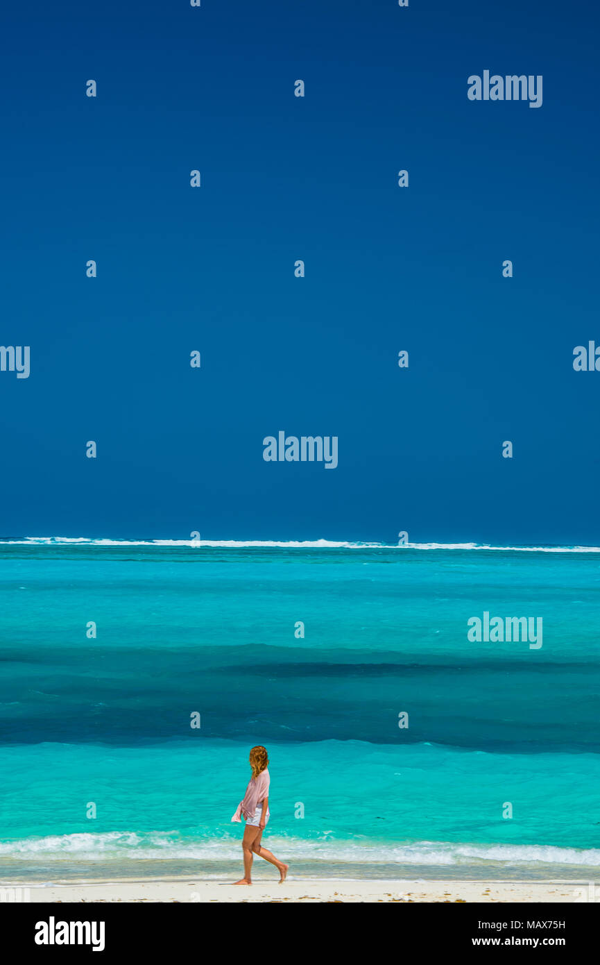 Donna che cammina lungo una spiaggia tropicale idilliaco nelle Isole Turks e Caicos, dei Caraibi con sabbia dorata e un azzurro oceano blu concettuale del viaggio e Foto Stock