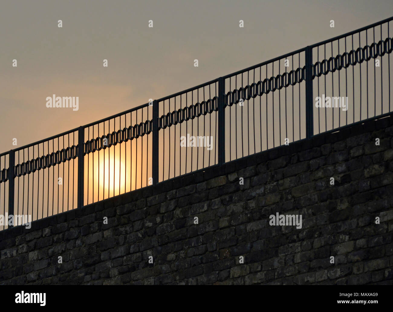 Il sole tramonta visto tra le ringhiere di recinzione presso la dinastia Ming parete reliquie park a Pechino in Cina Foto Stock