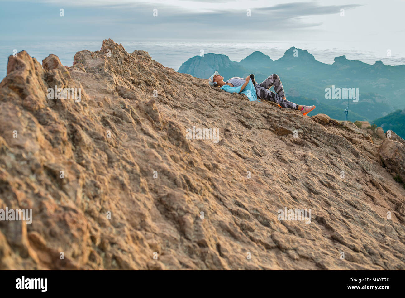 Escursionista femmina in appoggio sulla sommità di una ripida montagna alta con una fotocamera, picco di arenaria, Malibu, California Foto Stock