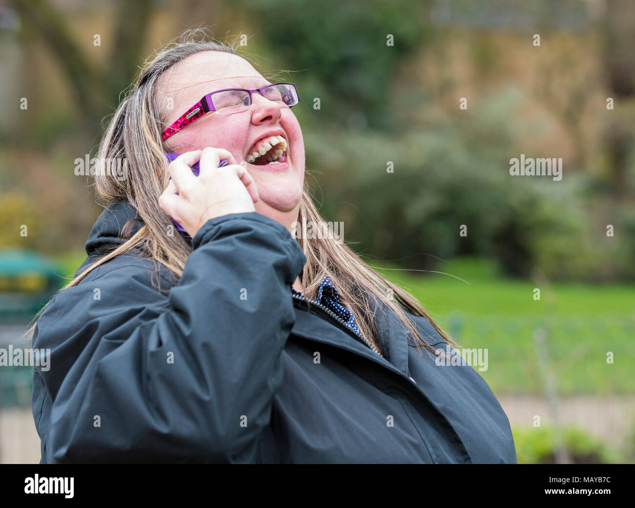 Giovane donna ridendo e guardando felice mentre godendo di una conversazione telefonica con un amico. Concetto di felicità. Avendo una risata. A ridere con gli amici. Foto Stock
