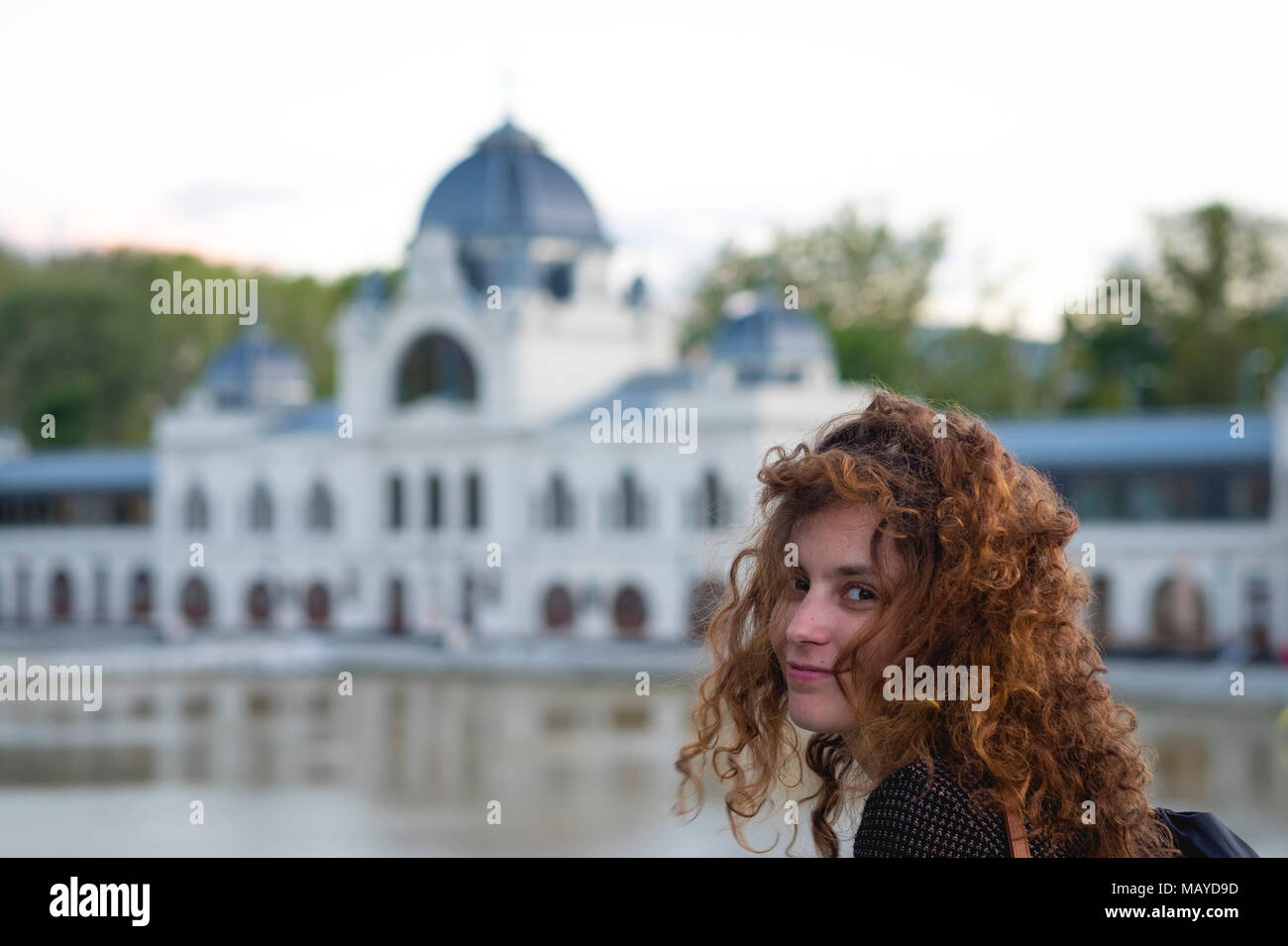 Carino redhead girl guardando la telecamera sorridendo con un bianco edificio barocco in background Foto Stock