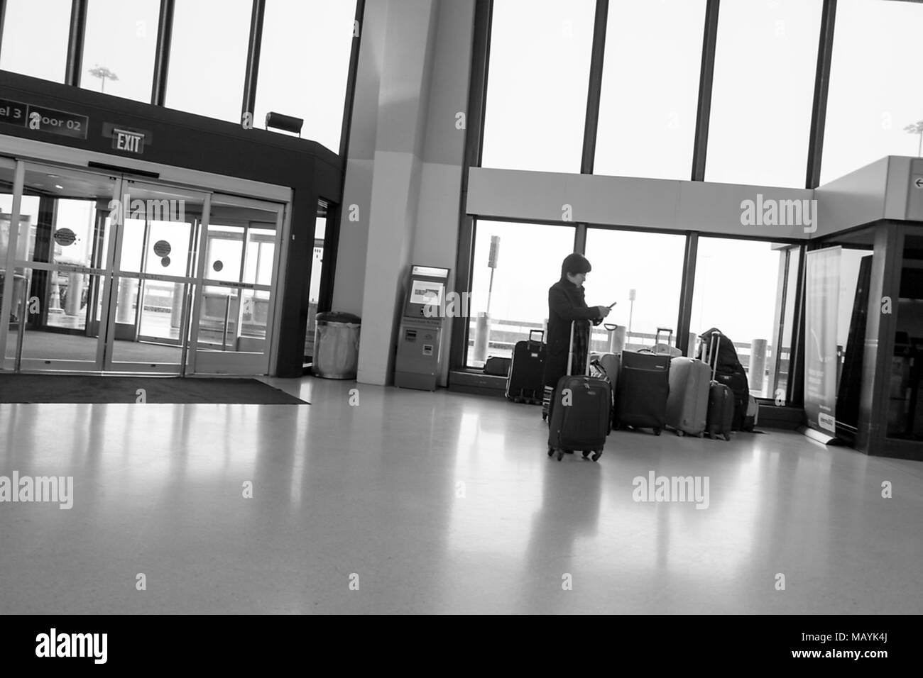 Un viaggiatore in stand con i bagagli e i controlli il suo telefono presso l'Aeroporto Internazionale di Newark (EWR) in Newark, New Jersey, Marzo 21, 2018. () Foto Stock