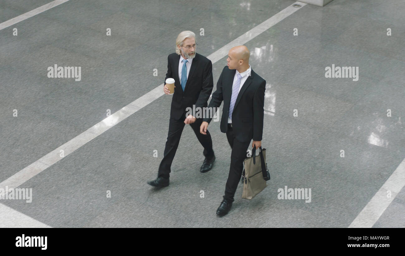 Angolo di alta vista di due dirigenti aziendali di parlare mentre si cammina attraverso la lobby di un ufficio moderno edificio. Foto Stock