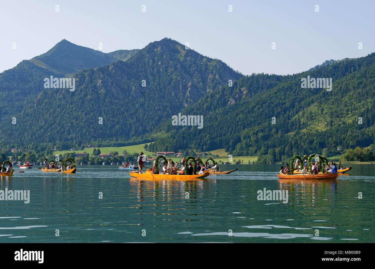 Uomini che indossano costumi tradizionali in addobbate a festa le piazze, barche in legno sul lago Schliersee, dietro Brecherspitze Foto Stock