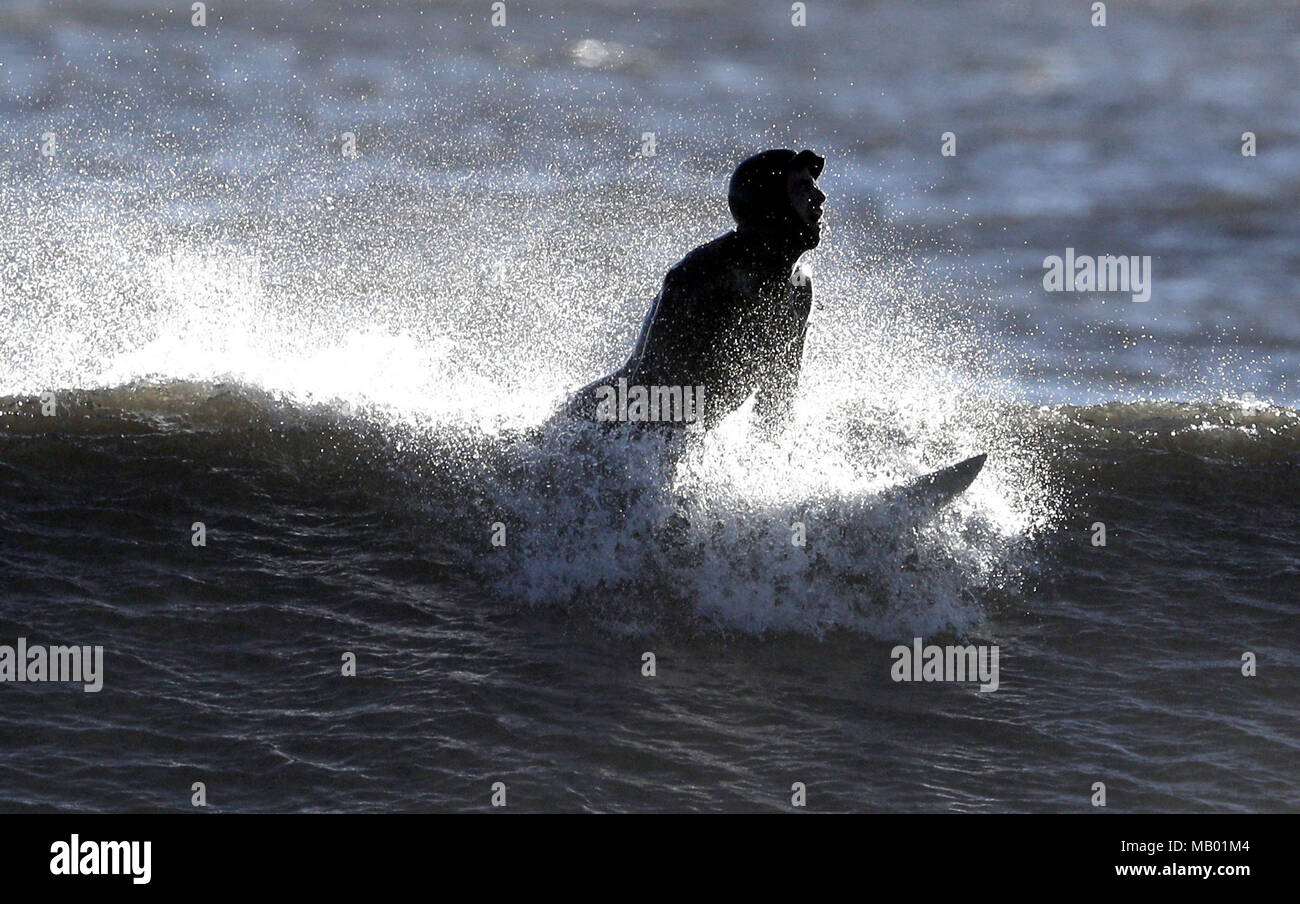 Questo surfer Cavalca le onde a Whitley Bay, Northumberland, dopo un wet marzo ha dato il via ad un caloroso inizio di aprile come forecasters predire a doppia cifra temperature attraverso la voce del Regno Unito verso il fine settimana. Foto Stock