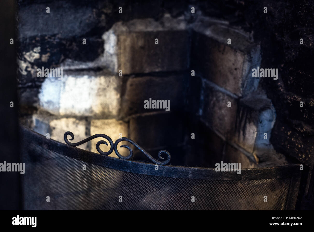 Un vecchio e rustico caminetto con mattoni sporca e ferro battuto fire schermo Foto Stock