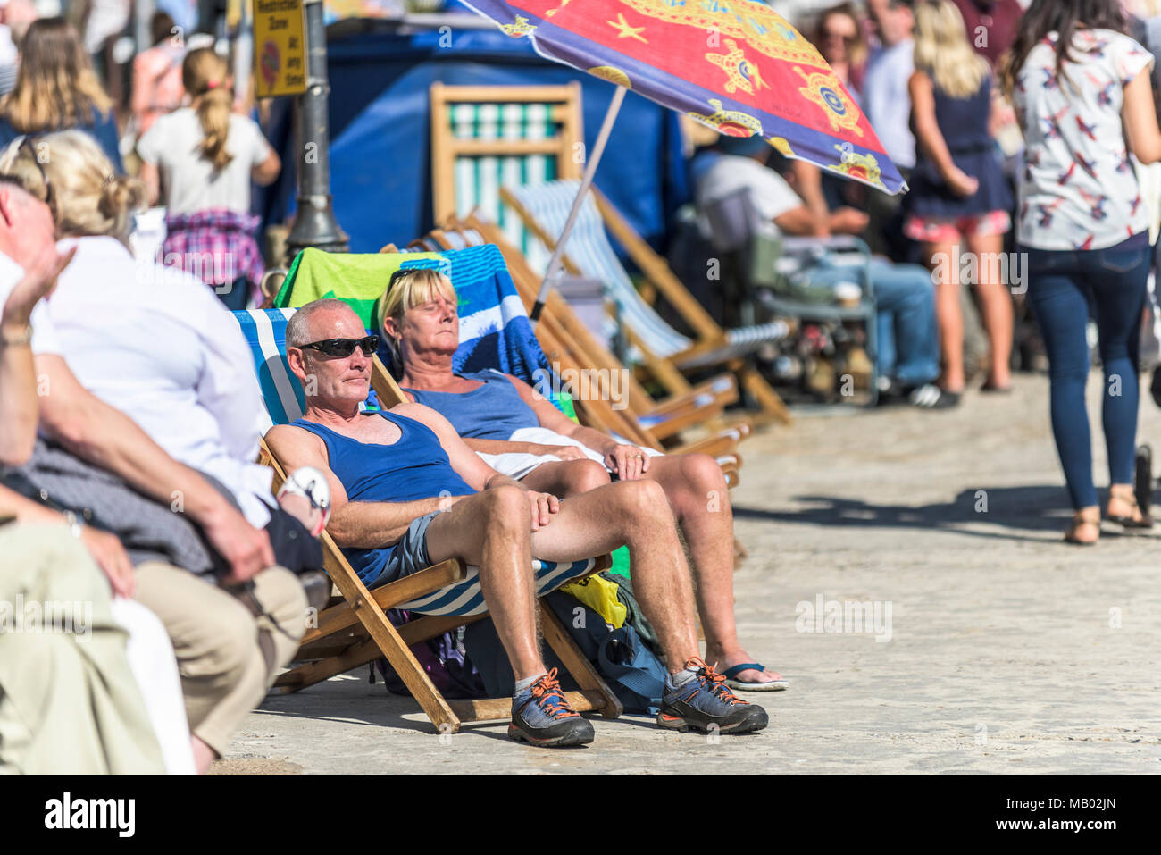 I villeggianti godendo il sole sulla banchina a St Ives Harbour in Cornovaglia. Foto Stock