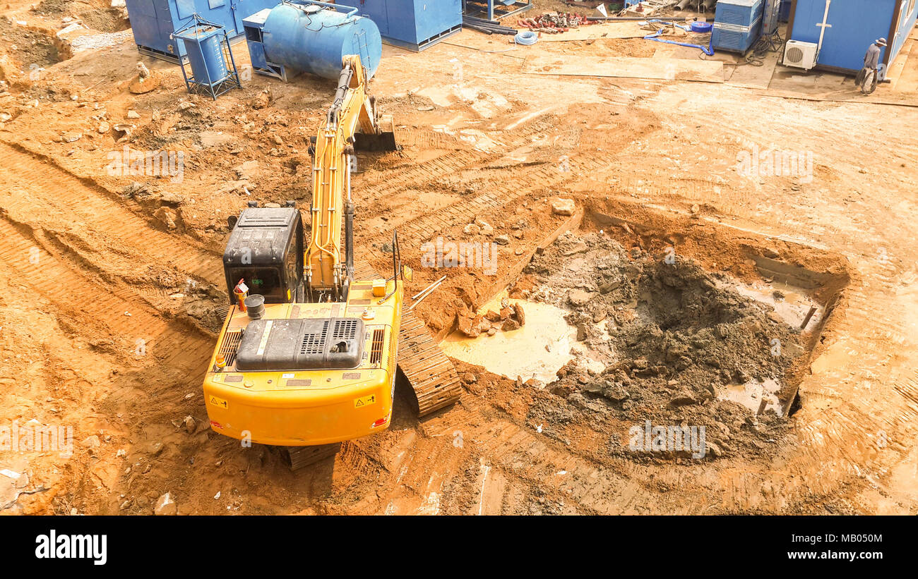 Vista aerea di escavatore cingolato inizia a scavare la preparazione di terra per costruire un condominio. via hoe funzionante. La preparazione del sito prima di costruire un condominio Foto Stock