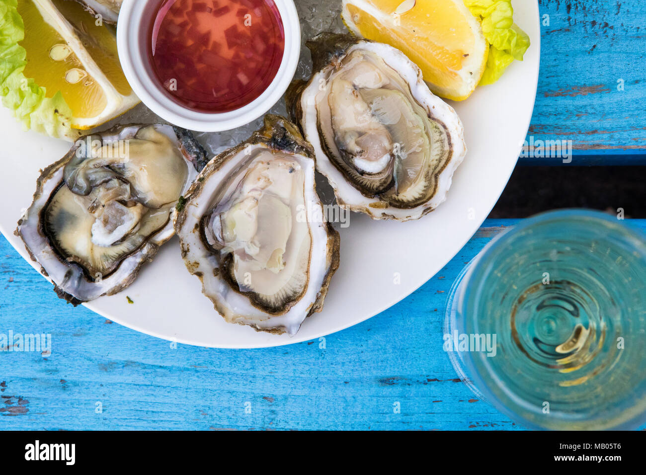 Ostriche e champagne con limone e cuneo mignette medicazione sulla piastra bianca sul blu vintage invecchiato tavolo. Foto Stock