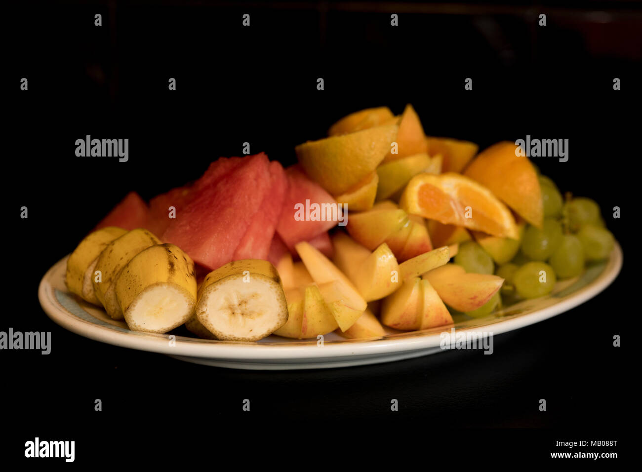 Un piatto di frutta fresca in pezzi su uno sfondo nero. Foto Stock