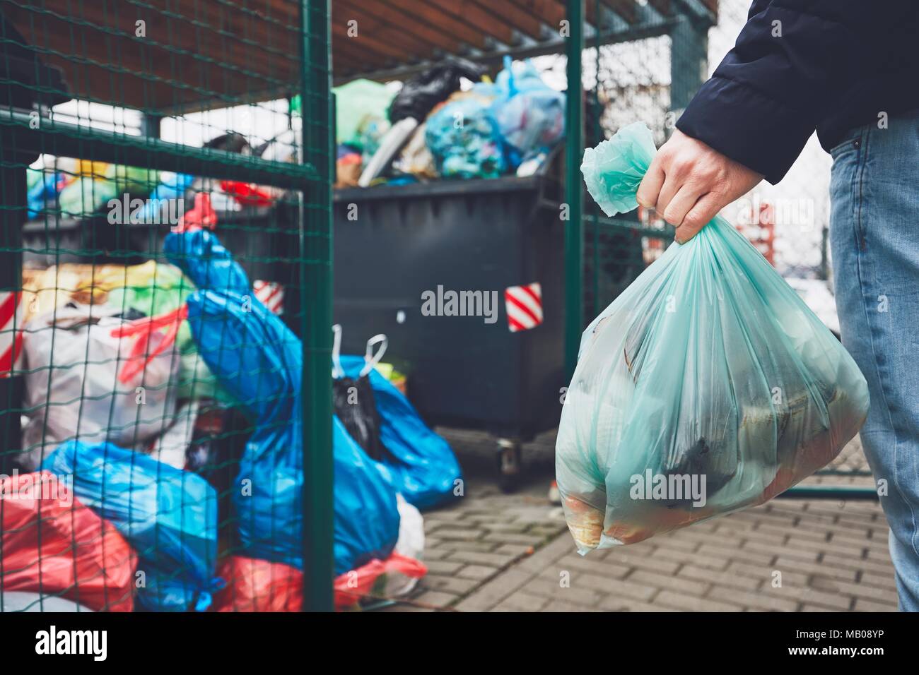 Mano con garbage contro il cestino pieno di lattine con sacchi per immondizia traboccare sul marciapiede. Foto Stock