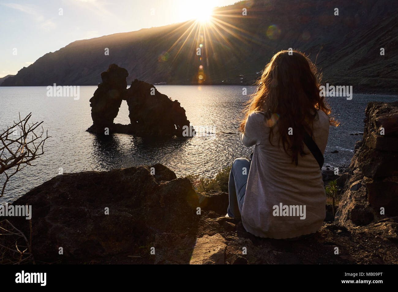 Donna seduta a guardare un tramonto vista panoramica di Roque de Bonanza isolotto di El Hierro, Isole Canarie, Spagna Foto Stock