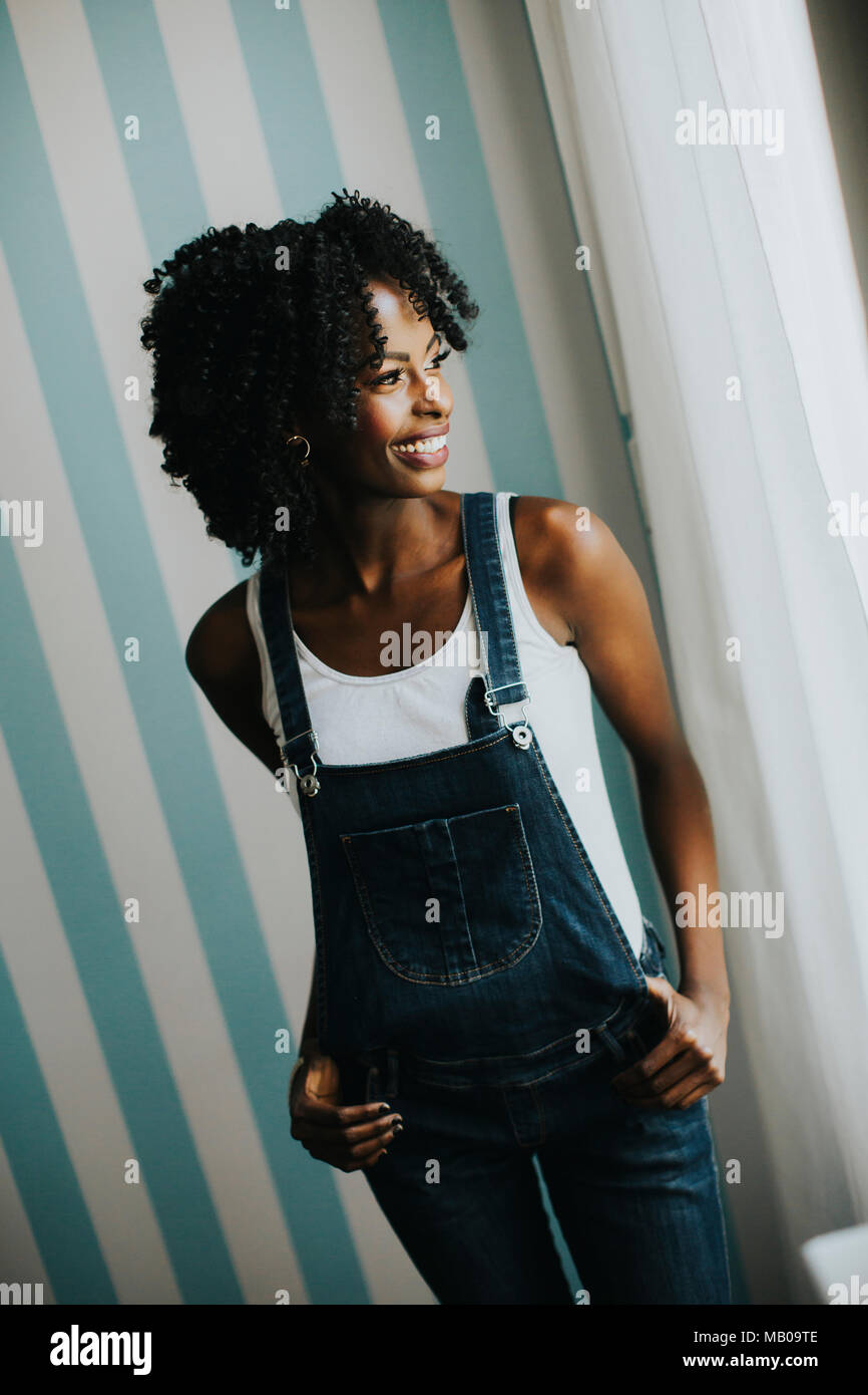 Piuttosto giovane americano africano che pongono la donna in jeans pantaloni da parete in camera Foto Stock