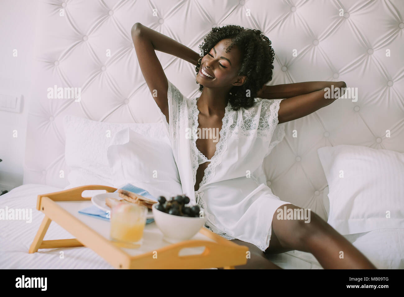 Sorridente americano africano donna avente una rilassante colazione a letto a casa Foto Stock