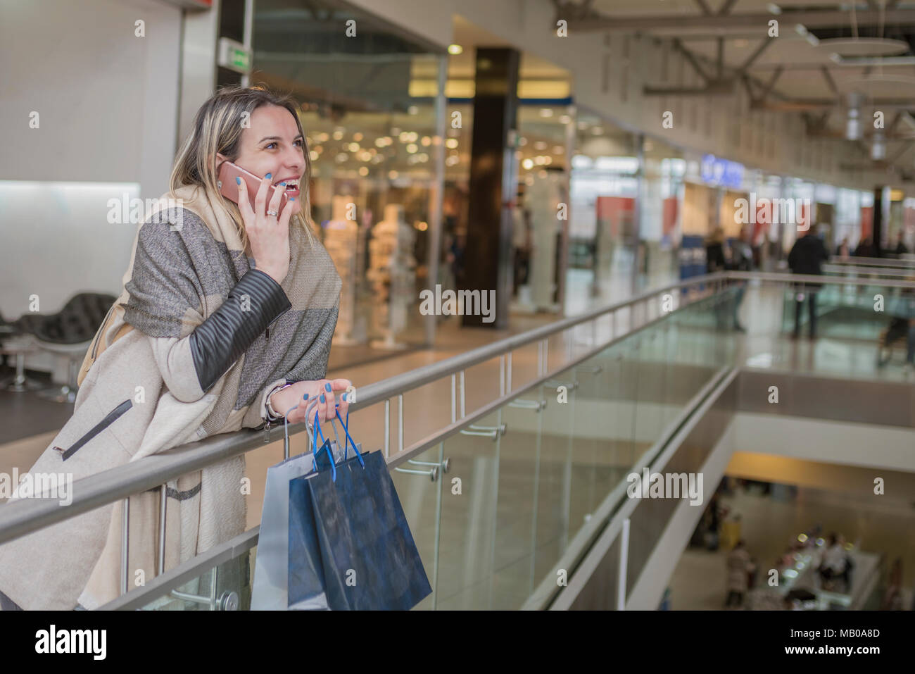 Ragazza sorridente parlando sul suo telefono cellulare in centro commerciale tenendo borse per lo shopping. Shopping Moda ragazza ritratto. La bellezza della donna con le borse della spesa Foto Stock