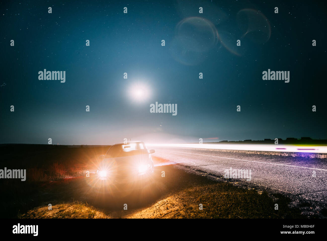 Notte Blu cielo stellato sopra di paese strada asfaltata in campagna. Sedan Parcheggio auto vicino alla strada asfaltata nella notte d'estate. Giallo auto luci e vista notturna Foto Stock