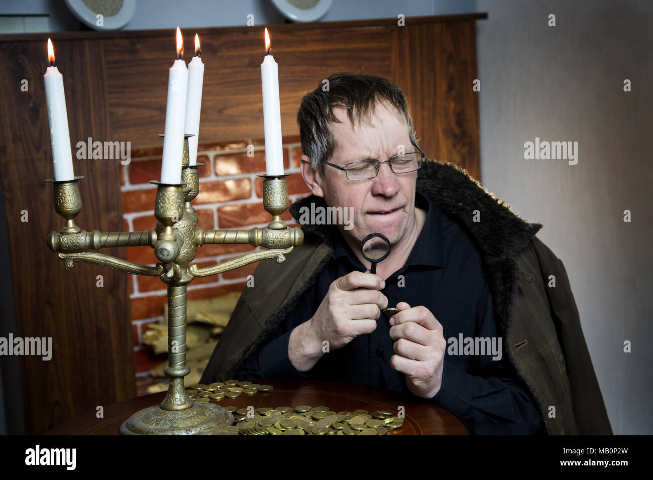 Un ricco avido uomo anziano guarda a monete sotto la luce di una candela che brucia. Foto Stock