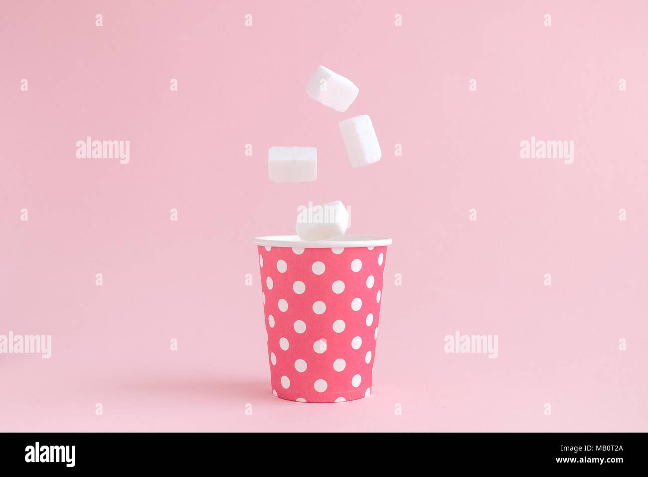 Zollette di zucchero che rientrano nel bicchiere di carta polka design contro di rosa pastello minima di sfondo concetto creativo. Foto Stock
