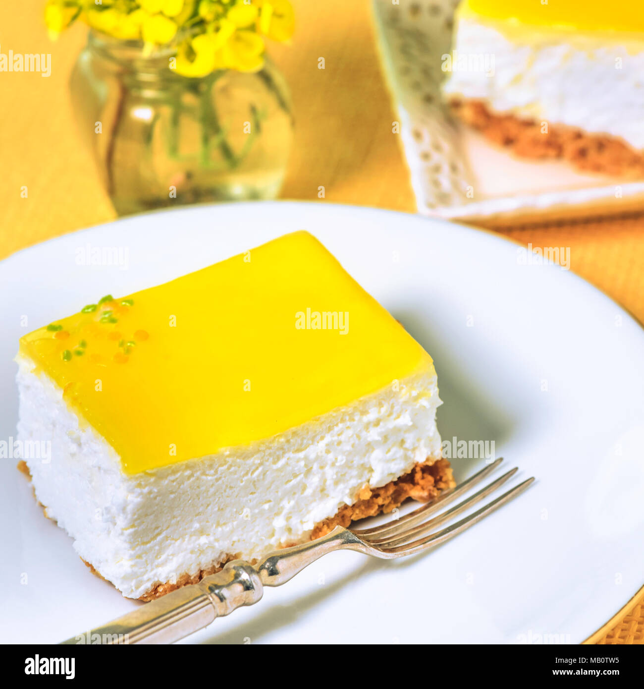 Fetta di Cheesecake al limone su un posto bianco con una forcella di argento e fiori gialli sfondo bokeh di fondo ad uno spazio di copia Foto Stock