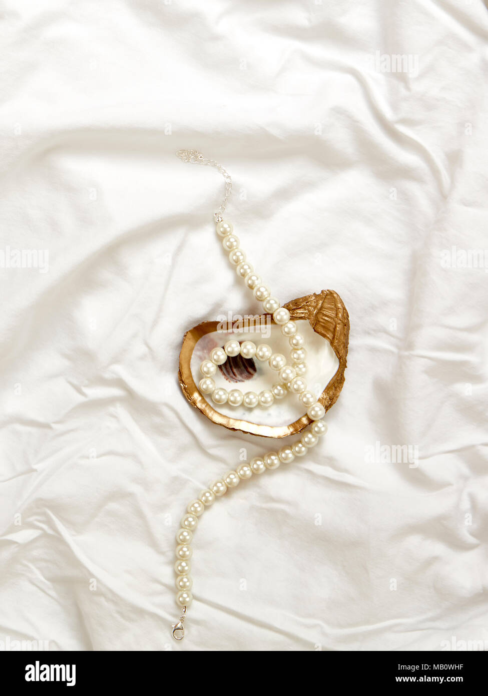 Oyster oro Gioielli piatto con collana di perle e oro anello di fidanzamento e matrimonio oro fascia su un tessuto bianco sullo sfondo Foto Stock