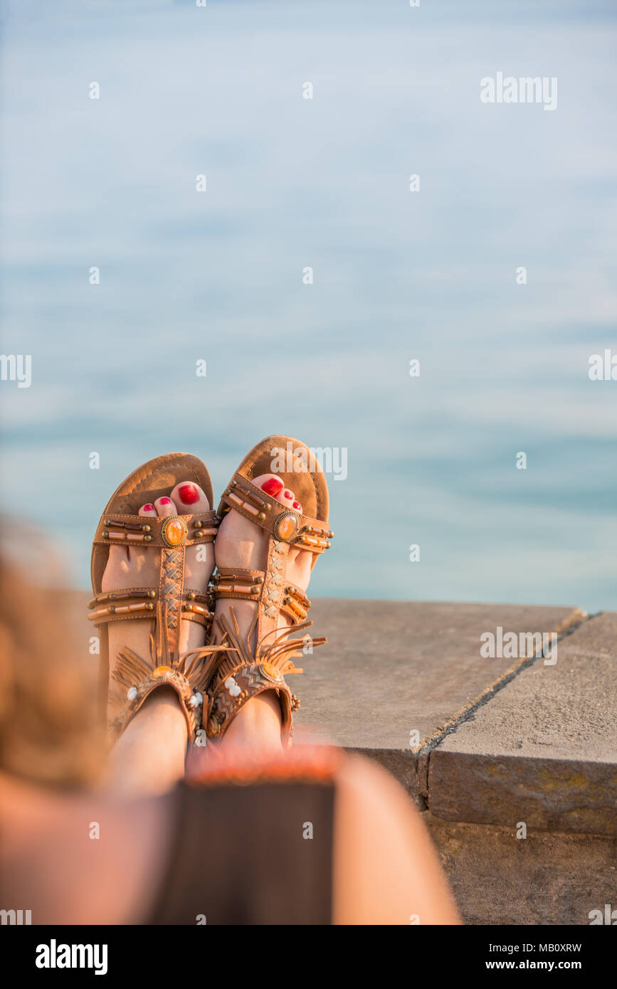 Close up della giovane donna in appoggio le gambe in sandali di cuoio a  riva del mare, vista posteriore con braccia e gambe di donna non  identificabili Foto stock - Alamy