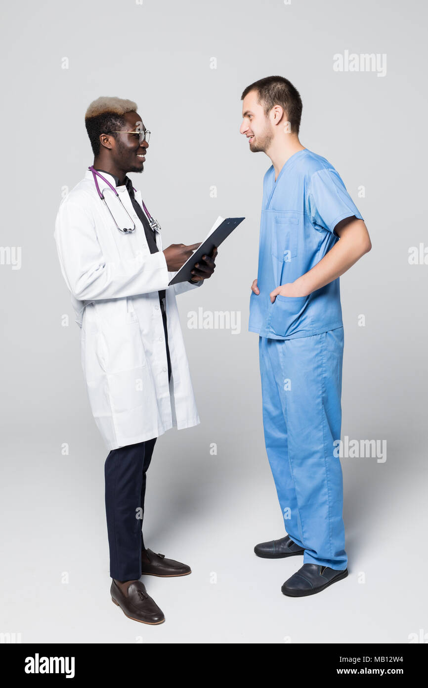 Due medici incontro e di consultarsi su sfondo grigio. Medico caucasica e afroamerican medico parlando abount pacient su grigio Foto Stock