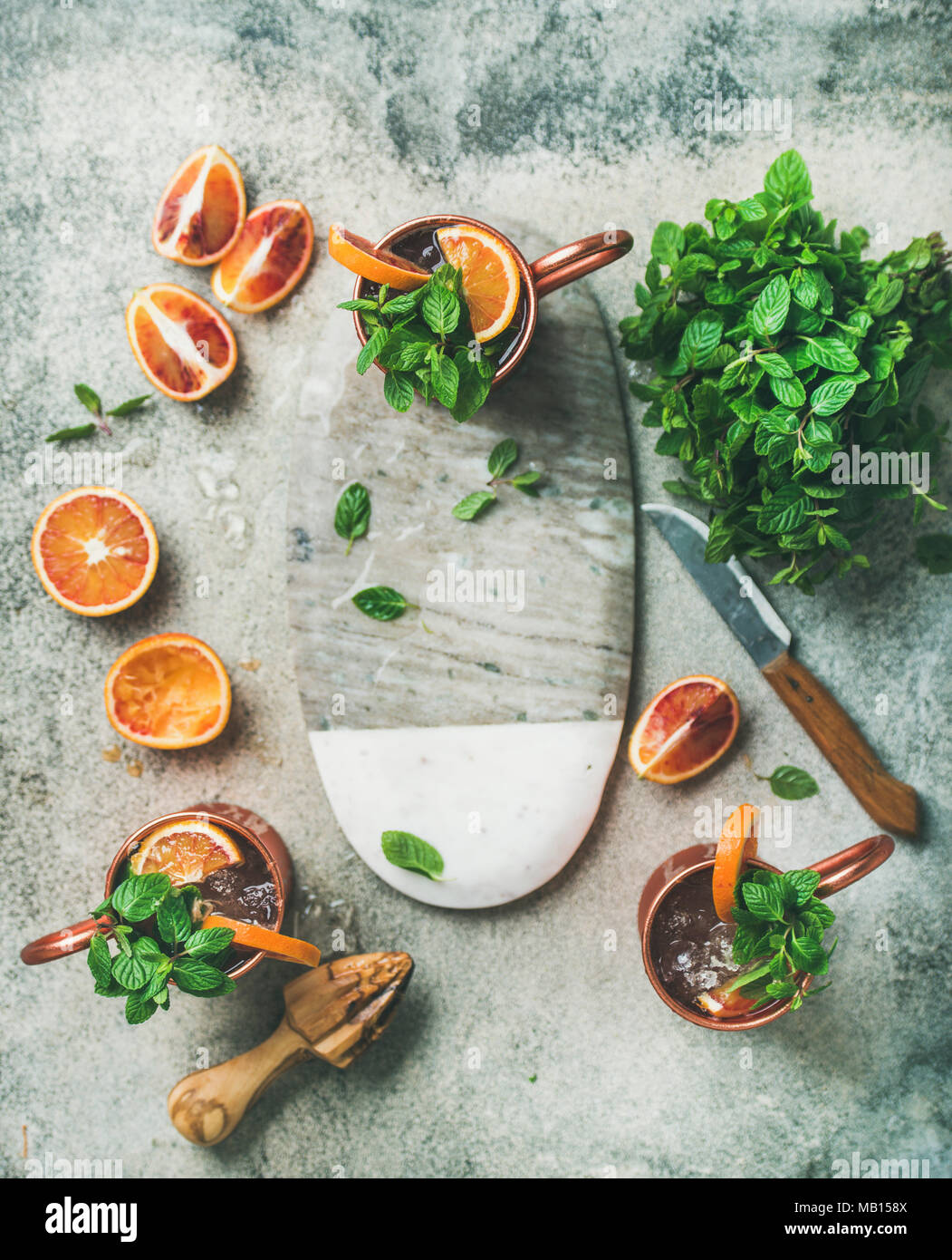 Arancio sanguigno Moscow mule cocktail alcolici con foglie di menta fresca e ghiaccio in tazze di rame e di pensione in centro su cemento grigio Sfondo, spazio di copia Foto Stock