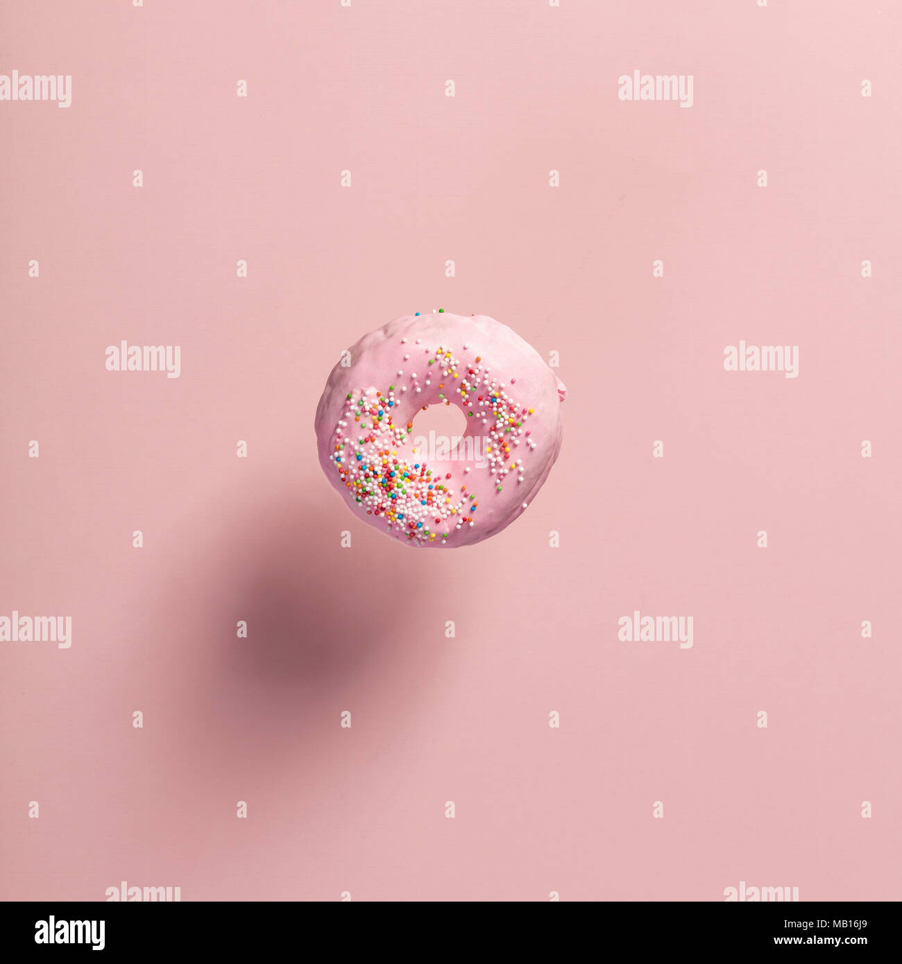 Ciambella rosa con un pizzico di caduta o battenti in movimento contro rosa sfondo pastello Foto Stock
