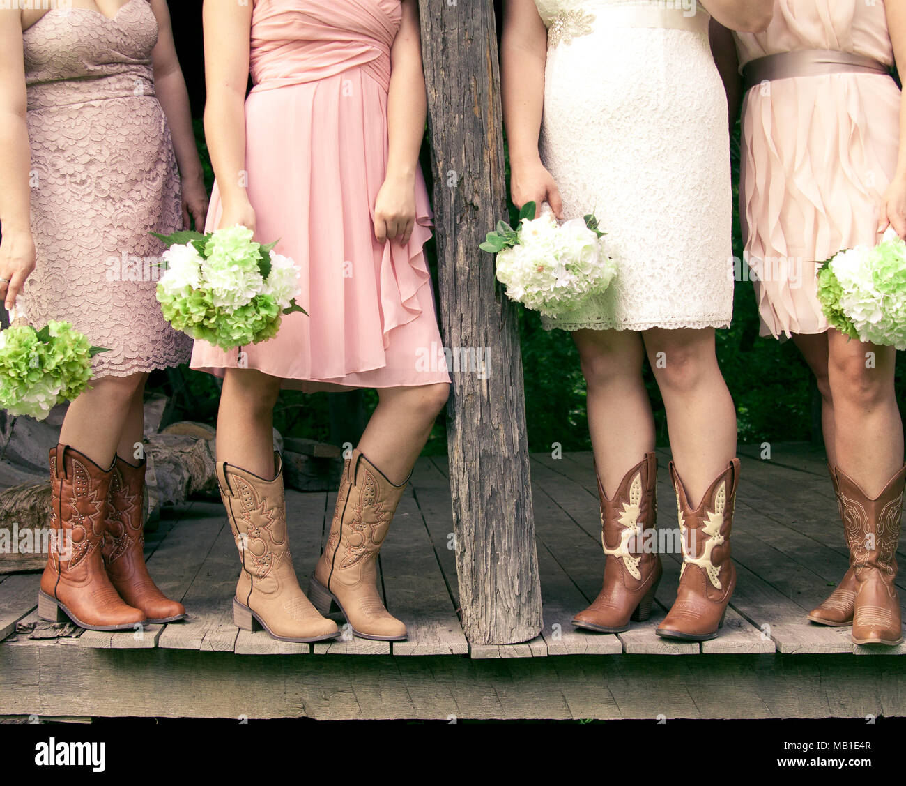Quattro damigelle con mazzi di fiori e di indossare gli stivali da cowboy in un paese di nozze a tema Foto Stock