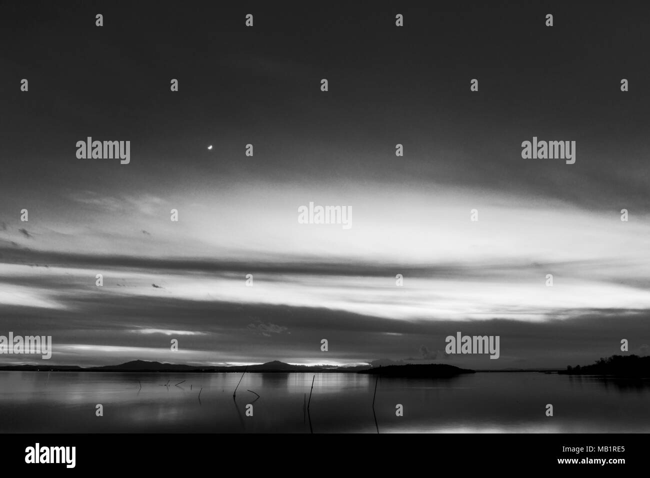 Bellissima vista del lago Trasimeno (Umbria, Italia) al tramonto, con toni del bianco e del nero e la luna nel cielo Foto Stock