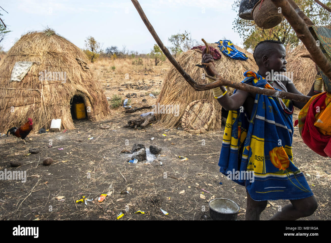Omorate, Etiopia - Gennaio 24, 2018: una donna dalla tribù dei Mursi in posa per un ritratto vicino ad un albero con le tradizionali case dei Mursi in Etiopia Foto Stock