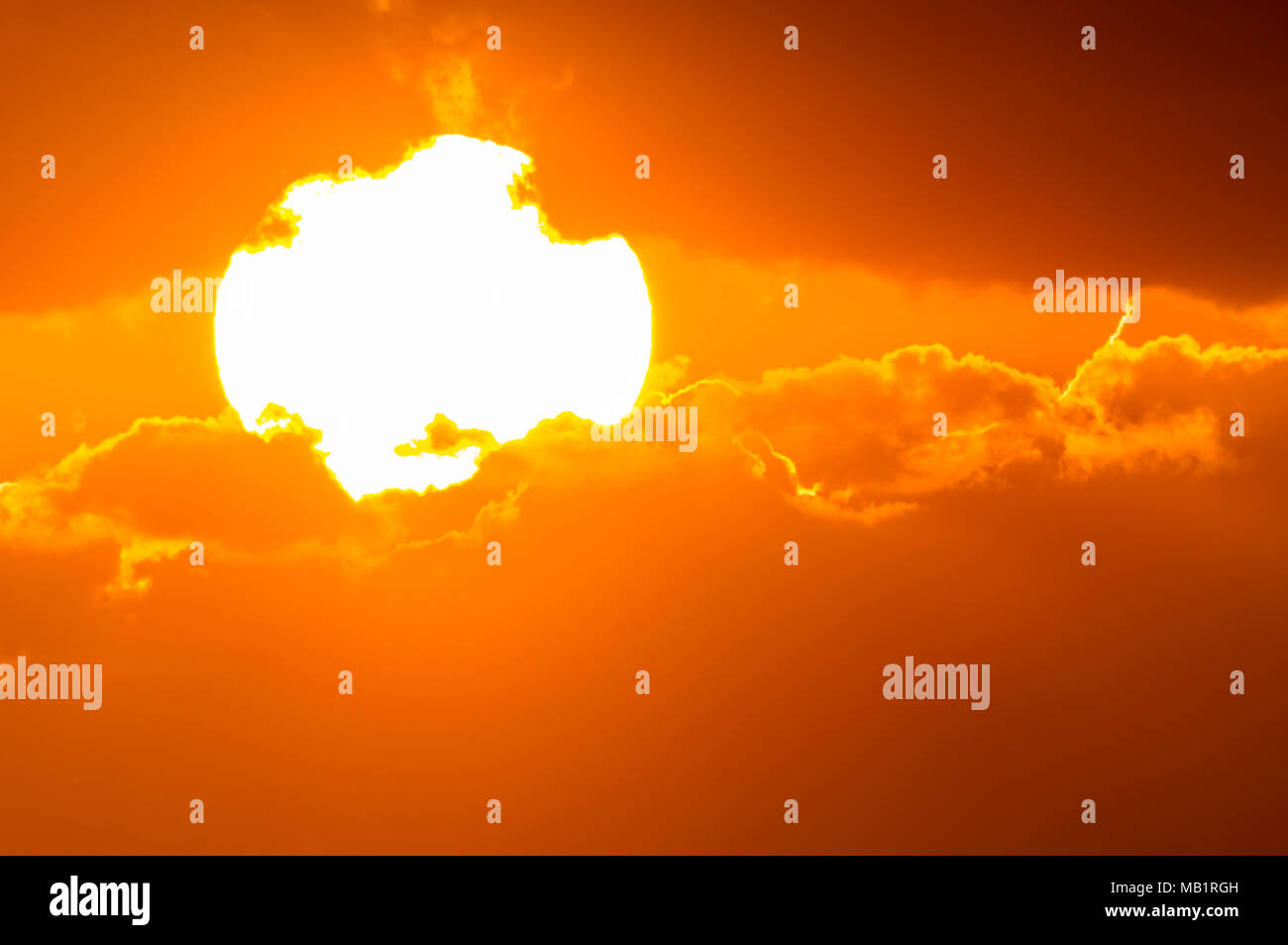 Primo piano del incandescente sole luminoso basso nel cielo, parzialmente coperto dalle nuvole poco prima del set. Foto Stock