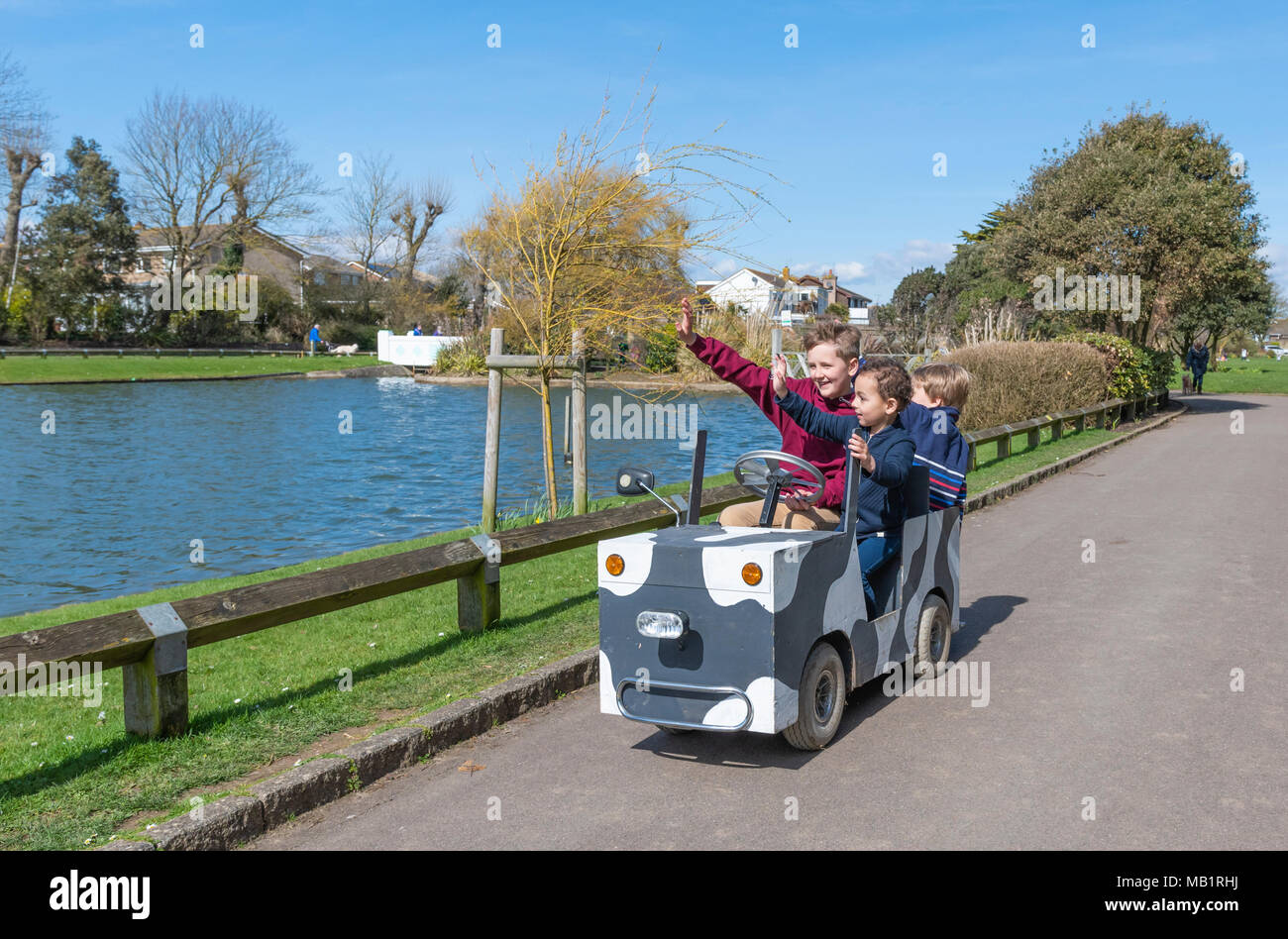 I bambini in sella a un giro sul bambino motorizzata il veicolo in un parco mentre sventolano a persone nel Regno Unito. Foto Stock