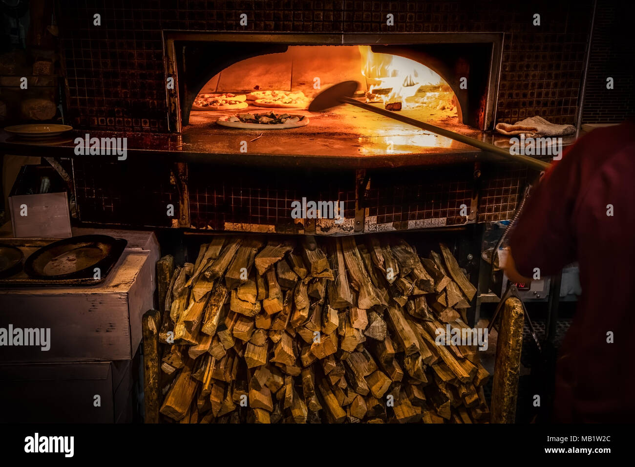 La cottura della pizza in forno a legna per la pizza con abbondanza di carburante al di sotto. Foto Stock La cottura della pizza in forno a legna per la pizza con abbondanza di carburante al di sotto. Foto Stock