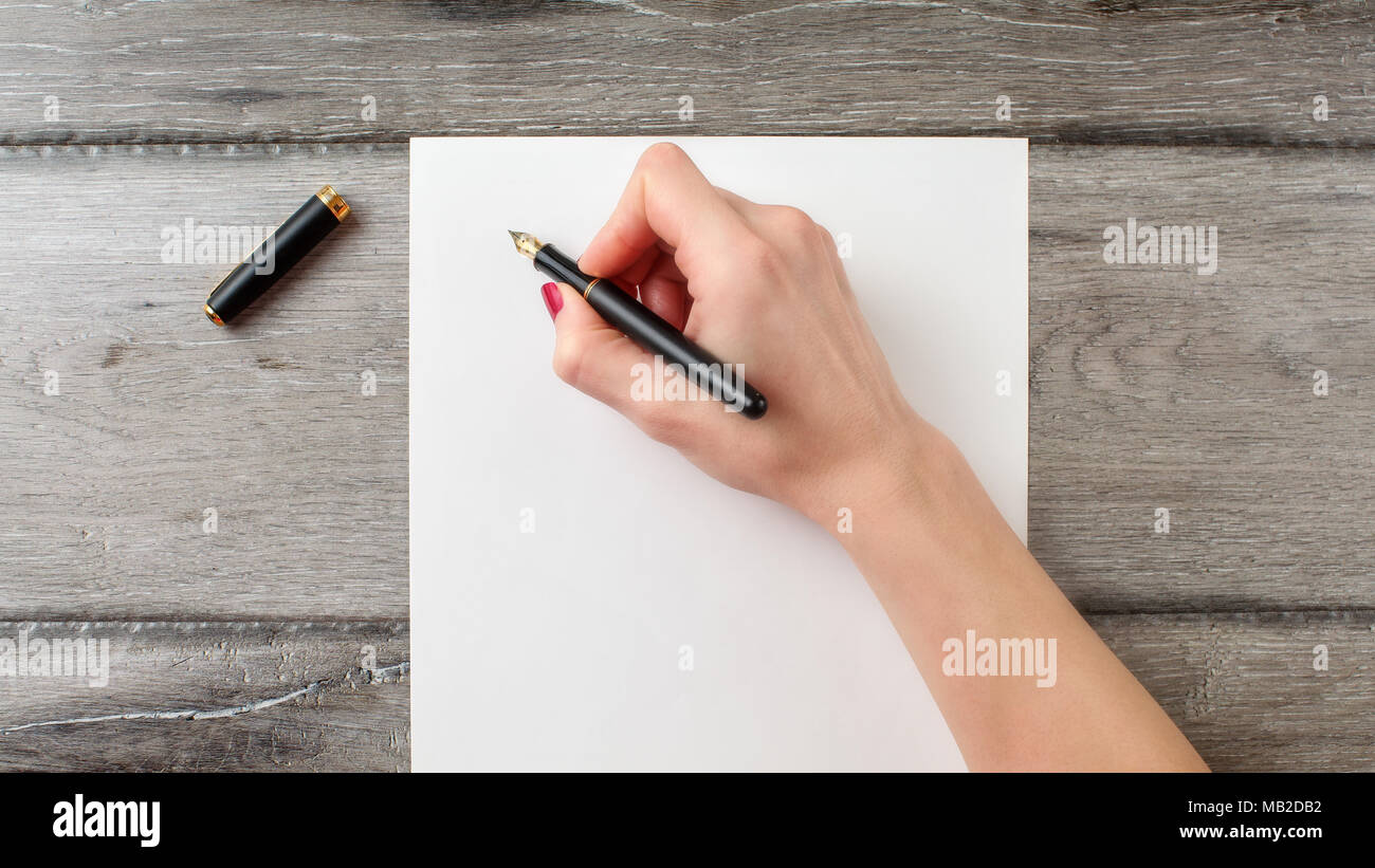 Donna di mano azienda nero penna stilografica pronti a scrivere su carta bianca su grigio scrivania in legno Foto Stock
