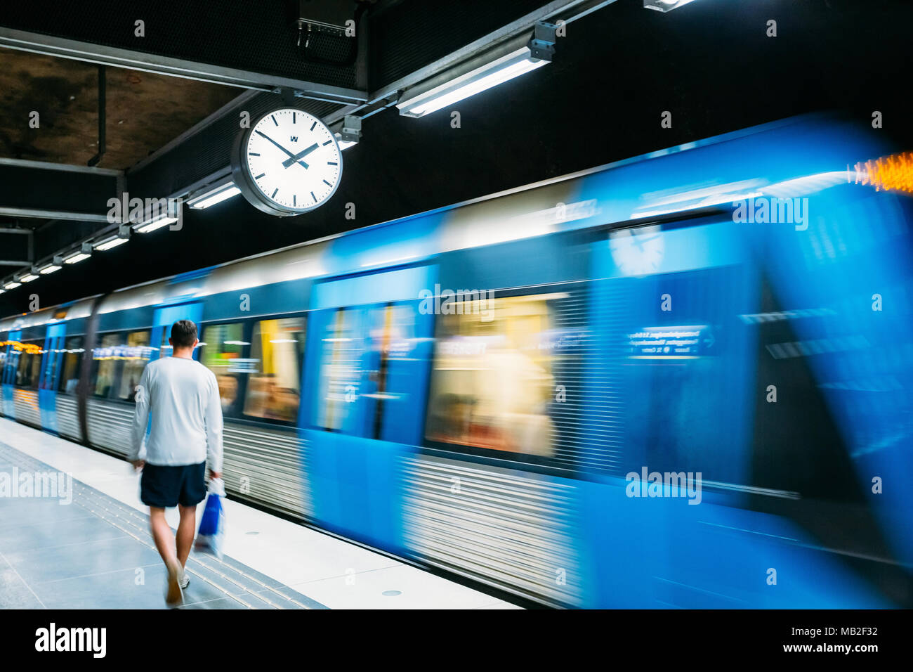 Stoccolma, Svezia - 30 luglio 2014: uomo a camminare nei pressi di illuminato moderna stazione della metropolitana Stazione della Metropolitana in blu e grigio con movimento del treno. Foto Stock