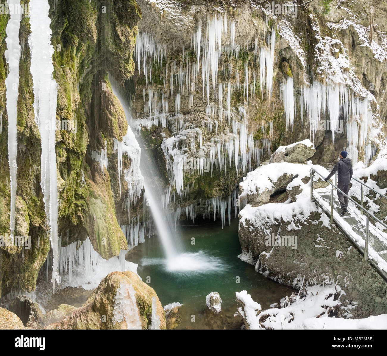 Escursionista uomo in piedi sul ponte godendo di ghiaccioli e cascata sul trekking invernale escursione. Hinanger cascata, Allgau, Germania. Foto Stock