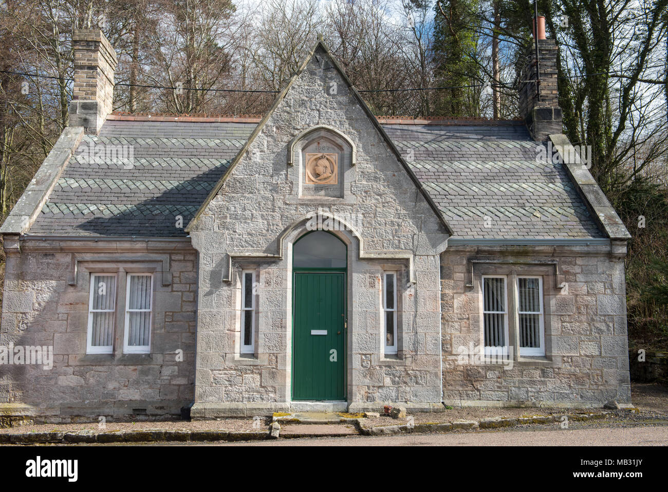 Grazioso piccolo cottage in pietra dall'architettura simmetrica, porta verde e due camini annidati ai margini di un bosco nel Regno Unito Foto Stock