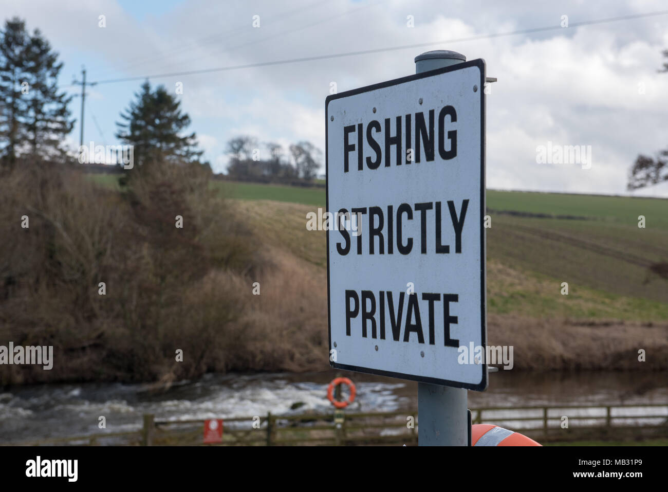Cartello “Fishing Strictly Private” affisso accanto a un fiume rurale o a un ruscello nella campagna del Regno Unito, con campi ondulati e alberi sullo sfondo Foto Stock
