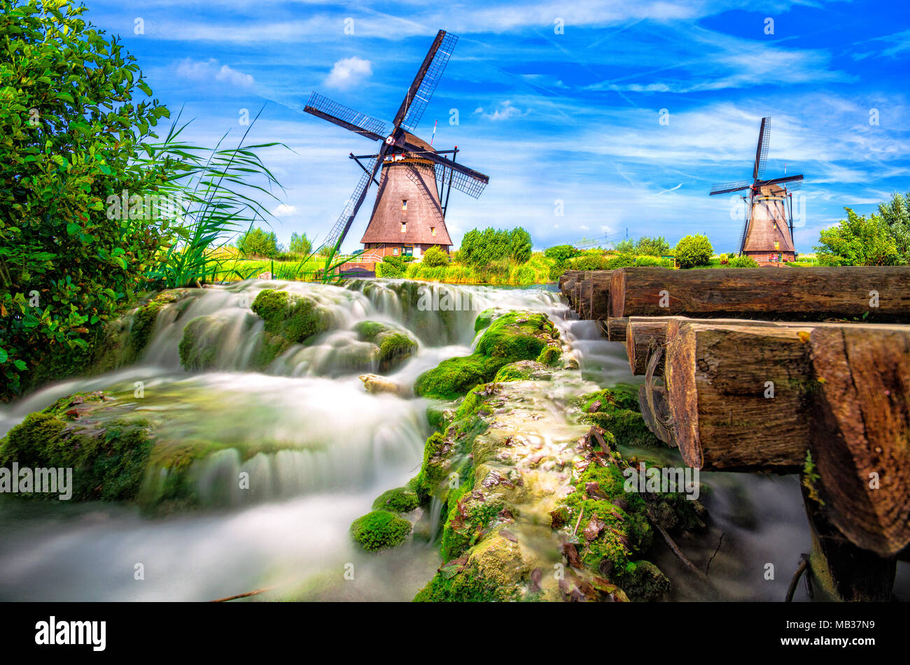 Villaggio Tradizionale al tramonto, con mulini a vento olandese, il ponte e il fiume, Holland, Paesi Bassi. Foto Stock