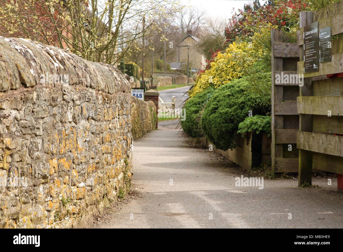 Inglese e pittoresco villaggio idilliaco a piedi in Oxfordshire, Regno Unito con muro di pietra, alberi e la vista della strada in distanza Foto Stock