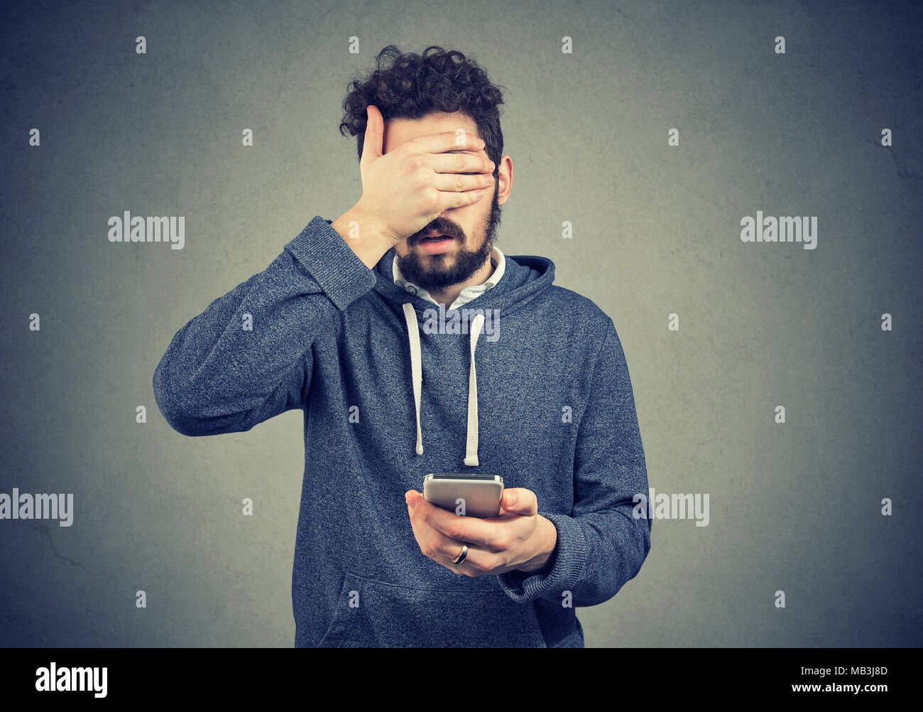 Triste spiacevoli giovane con il telefono cellulare che copre con la mano il suo volto Foto Stock