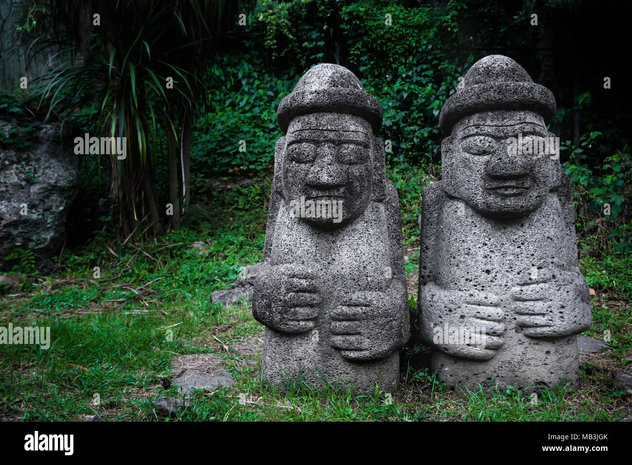 Due Dol Hareubang statue con cappelli e le mani sulla pancia in verde scuro foresta, Seogwipo, Jeju Island, Corea del Sud Foto Stock