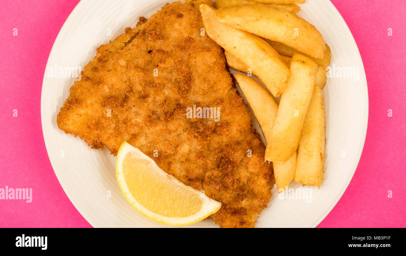 Popolare tradizionale pesce e patatine contro un sfondo rosa con una fettina di limone Foto Stock