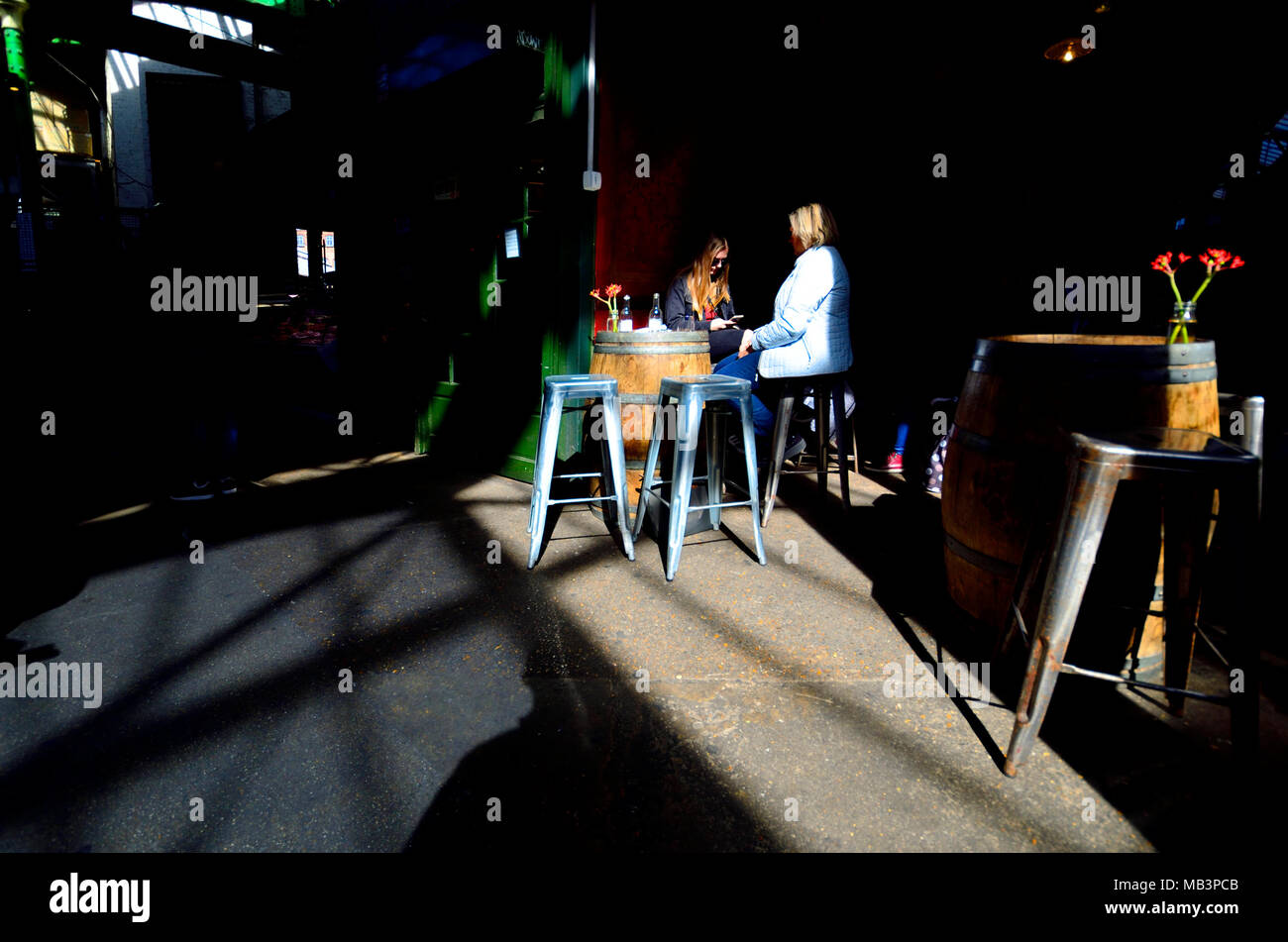 Londra, Inghilterra, Regno Unito. Due donne aventi un drink nel mercato di Borough, uno utilizzando il suo telefono cellulare Foto Stock